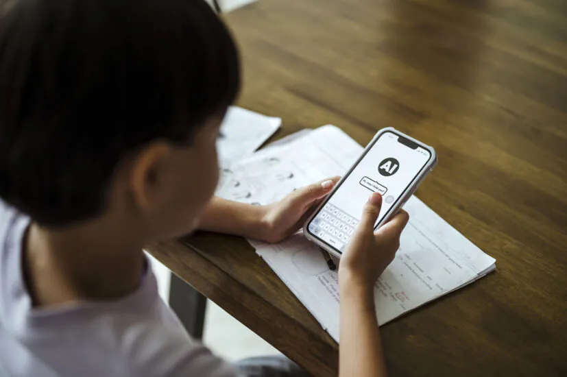 A young student interacts with an AI chatbot on a smartphone while studying. TITLE: